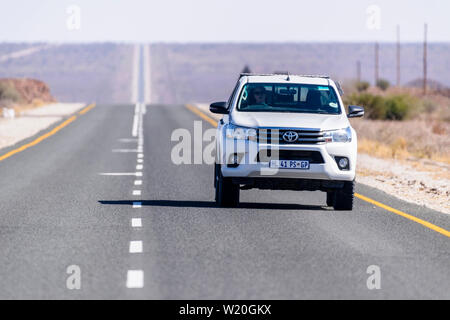 White Toyoya Hilux pick-up truck guidando lungo una retta molto e a lungo su strada asfaltata attraverso il deserto del Kalahari, Namibia Foto Stock