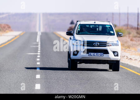 White Toyoya Hilux pick-up truck guidando lungo una retta molto e a lungo su strada asfaltata attraverso il deserto del Kalahari, Namibia Foto Stock