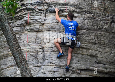 Un giovane maschio scalatore lavora il suo modo di una scogliera a battuta la molla Trail a Pilot Mountain State Park in North Carolina. Foto Stock