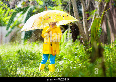 Bambini che giocano sotto la pioggia sulla soleggiata giornata autunnale. Kid sotto doccia pesante con anatra giallo ombrello. Ragazzino con anatroccolo scarpe impermeabili. Wel in gomma Foto Stock