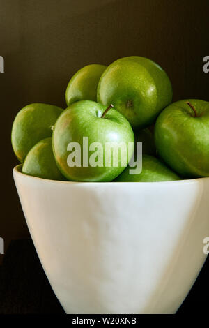 Verde Granny Smith mele di cottura in una ciotola bianco contro un sfondo marrone. Foto Stock