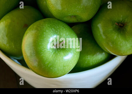 Un close-up immagine di un gruppo di verde Granny Smith mele di cottura in una ciotola bianco dal di sopra. Foto Stock