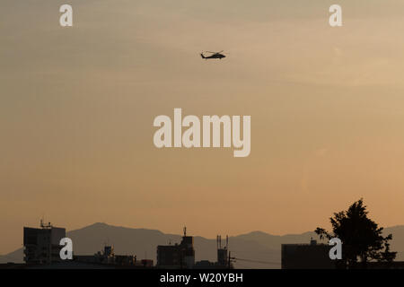 Un elicottero Sikorsky SH-60 Seahawk in silhouette, che vola al tramonto dalla Naval Air Facility Atsugi, base aerea, Kanagawa, Giappone. Foto Stock