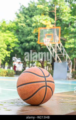 In pelle di basket sulla sedia in legno con goccioline di acqua sfondo campo da pallacanestro e un parco. Foto Stock