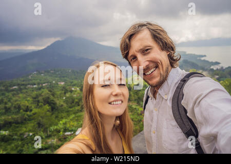 Uomo e donna che fa selfie sullo sfondo del vulcano Batur e Agung mountain view al mattino da Kintamani, Bali, Indonesia Foto Stock