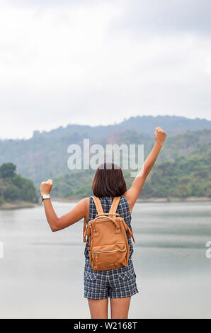 Donne sollevare le braccia e la spalla zaino sullo sfondo delle montagne e acqua a Wang Bon dam ,Nakhon Nayok in Thailandia. Foto Stock