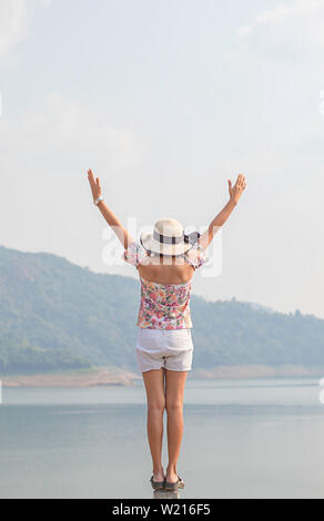 Donne alzando le braccia e sullo sfondo le montagne e acqua a Khun Dan Prakan Chon Dam ,Nakhon Nayok in Thailandia. Foto Stock