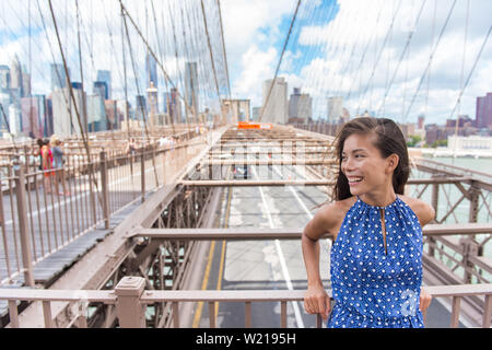 Bella giovane donna asiatica verticale sul ponte di Brooklyn, New York City NYC, Manhattan STATI UNITI D'AMERICA. Sorridente turistico in vestito blu facendo viaggio estivo in punto di riferimento urbano. Foto Stock