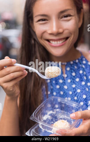 Donna asiatica di mangiare il cibo giapponese in Asia Travel. Gara di misto ragazza cinese tenendo una forcella con una sfera di mochi - torta di riso snack dessert con frutta o di fagioli rossi ricoperta di zucchero in polvere o cocco grattugiato. Foto Stock
