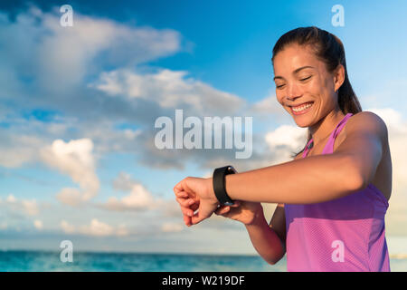 Ragazza attivo utilizzando il tracker di fitness smart watch jogging sulla natura estiva all'aperto osservando i dati sanitari durante la attività sportiva toccando lo schermo del suo smartwatch. Foto Stock