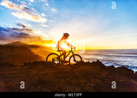 Mountain bike mtb ciclista donna ciclismo su pista ciclabile sulla costa al tramonto. Persona sulla bicicletta da mare in abbigliamento sportivo con bicicletta godendo di un sano stile di vita attivo nella splendida natura. Foto Stock