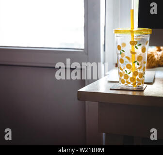 Un bicchiere con una cannuccia con dipinto di limoni sulla scrivania di un ufficio di casa vicino al computer. Foto Stock