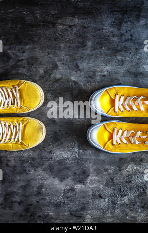 Giallo antico indossato sporchi strappati e scarpe da ginnastica e nuove sneakers al buio su un sfondo grunge. vista dall'alto. Spazio di copia Foto Stock