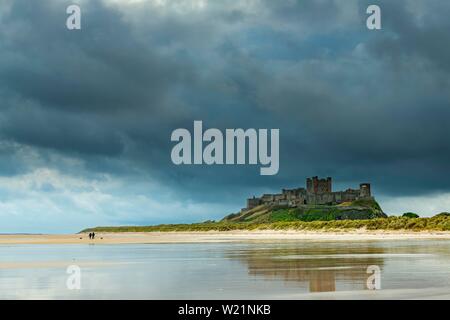 Appartamento costa sabbiosa con il castello di Bamburgh e riflesso nell'acqua con nuvole scure, Bamburgh, New Castele upon Tyne, Northumberland, Gran Bretagna Foto Stock