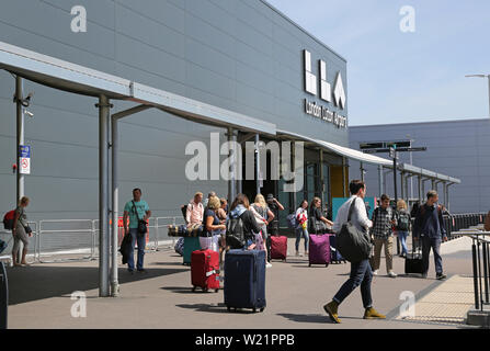 L'aeroporto London Luton, Regno Unito. I passeggeri con bagaglio approccio l'ingresso del nuovo edificio del terminal. Mostra il nuovo logo airport sopra. Foto Stock