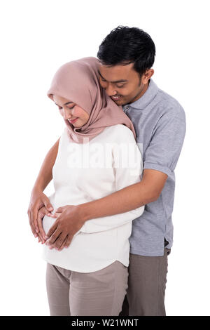 Incinta moglie musulmana appoggiata sul romantico marito al torace e mano prendere forma di cuore sulla pancia in gravidanza con sfondo isolato Foto Stock