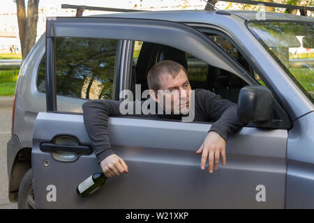 Autista ubriaco con una bottiglia di alcool cade fuori della porta della propria autovettura Foto Stock