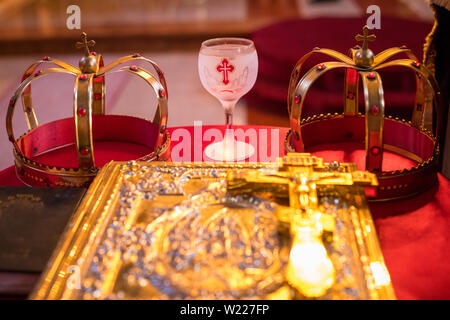 Due corone e bicchiere di vino rosso sul tavolo preparato per il matrimonio. Chiesa ortodossa nozze accessori. Foto Stock