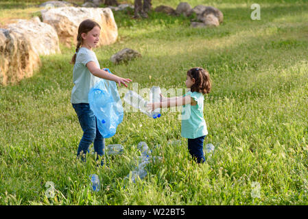 Carino bambine pulizia lettiera in plastica sull'erba. Bambini I volontari la pulizia di lettiera e mettere la bottiglia di plastica nel sacchetto di riciclaggio. Foto Stock