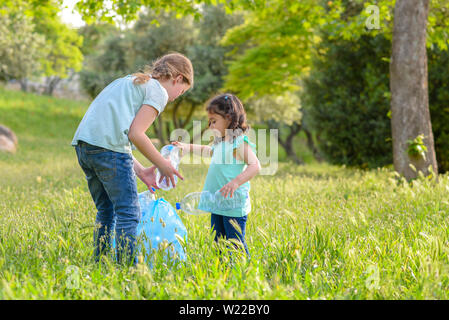 Inquinamento di plastica sulla terra. Picking Cildren la bottiglia di plastica da erba nel parco inquinati. Foto Stock