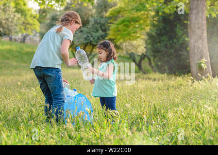 Bambine incassi di bottiglie di plastica a partire da erba. Bambini il prelievo di lettiera nella foresta . Foto Stock