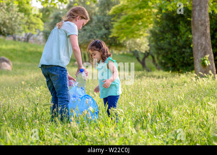 Carino bambine pulizia lettiera in plastica sull'erba. Bambini I volontari la pulizia di lettiera e mettere la bottiglia di plastica nel sacchetto di riciclaggio. Giornata mondiale dell'ambiente. Foto Stock