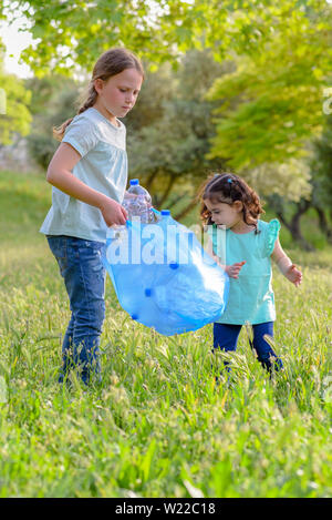 Carino bambine pulizia lettiera in plastica sull'erba. Bambini I volontari la pulizia di lettiera e mettere la bottiglia di plastica nel sacchetto di riciclaggio. La Giornata Mondiale dell Ambiente Foto Stock