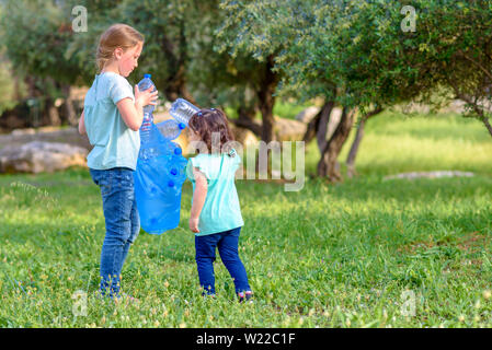 Carino bambine pulizia lettiera in plastica sull'erba. Bambini I volontari la pulizia di lettiera e mettere la bottiglia di plastica nel sacchetto di riciclaggio. Giornata mondiale dell'ambiente. Foto Stock