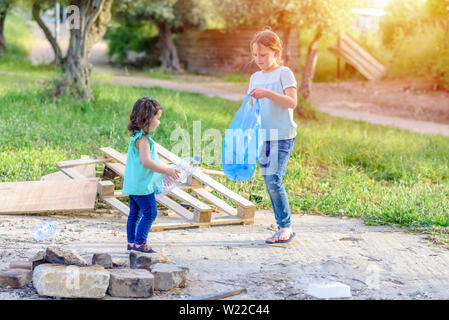 Carino bambine pulizia lettiera in plastica sull'erba. Bambini I volontari la pulizia di lettiera e mettere la bottiglia di plastica nel sacchetto di riciclaggio. Giornata mondiale dell'ambiente. Foto Stock