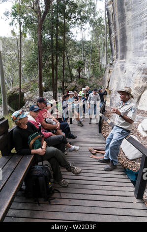 Una guida Aborigena dà un talk sullo sfondo del ben conservato rock Aborigena Arte stencil per i visitatori. Stencil arte sito è ritenuto t Foto Stock