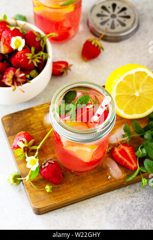 Limonata Fresca con srtawberries, limoni e ghiaccio su una pietra di luce o tavola di ardesia. Foto Stock