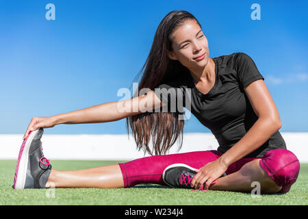 Donna Fitness stretching di una gamba toe-touch stretch esercizio posteriori della coscia e muscoli gluteo si allunga. Sportivo atleta asiatica esercizio seduta piegare in avanti le gambe esercizio sull'erba nella soleggiata palestra all'aperto. Foto Stock