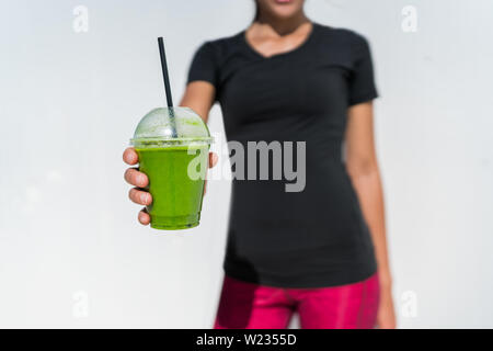 Mangiare sano stile di vita atleta fitness donna bere verde bicchiere per frullato vegano per la perdita di peso dieta. Prima colazione con succhi di frutta e verdura trend. Persona che mostra un contenitore di plastica a outdoor cafe o succo di bar. Foto Stock