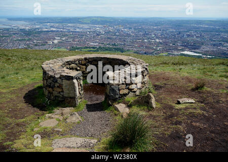 La città di Belfast da pietre a secco rifugio sulla montagna nera Ridge Trail nella contea di Antrim, Irlanda del Nord, Regno Unito. Foto Stock