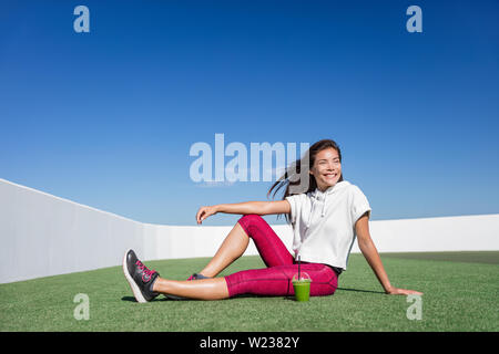 Un sano fitness donna asiatica bere frullato verde. Felice rilassante atleta sportivo durante il training di forza di rottura di allenamento in estate all'aperto godendo di un succo vegetale prima colazione al mattino nel activewear. Foto Stock