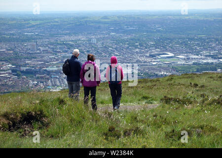 Tre i camminatori guardando verso il basso sulla città di Belfast dalla Montagna Nera Ridge Trail nella contea di Antrim, Irlanda del Nord, Regno Unito. Foto Stock