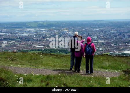 Tre i camminatori guardando verso il basso sulla città di Belfast dalla Montagna Nera Ridge Trail nella contea di Antrim, Irlanda del Nord, Regno Unito. Foto Stock