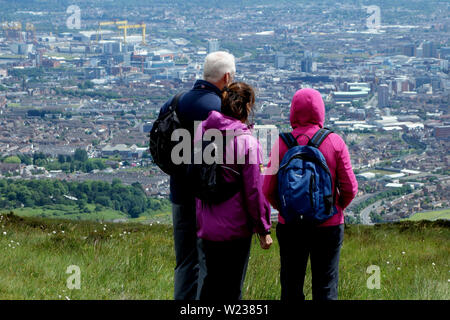 Tre i camminatori guardando verso il basso sulla città di Belfast dalla Montagna Nera Ridge Trail nella contea di Antrim, Irlanda del Nord, Regno Unito. Foto Stock