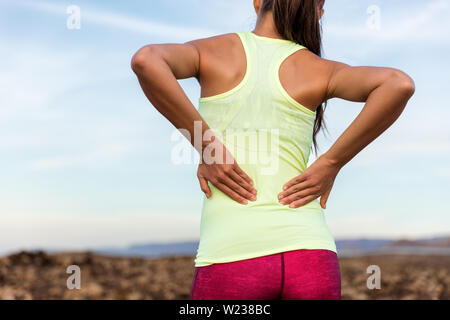 Trail Running runner con dolorose dolori alla parte inferiore della schiena o lesioni muscolo strained vicino alla colonna vertebrale. Atleta femminile da dietro su esterno premendo il corpo con le mani per i muscoli crampi indolenzimenti. Foto Stock