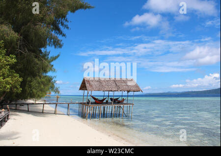 Stilt piattaforma con amache sopra l'acqua su una spiaggia tropicale in Raja Ampat in una giornata di sole. Foto Stock