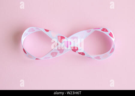 Simbolo di infinito fatto di cuore design contro il nastro rosa pastello minima di sfondo amore creativo concetto. Foto Stock