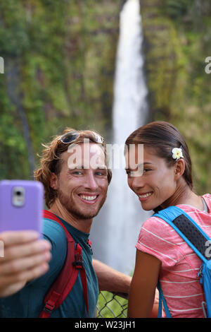 Hawaii giovane turista tenendo il telefono da viaggio selfie autoritratto con la fotocamera del telefono alle Hawaii, grandi isole, Akaka Falls. Felice allegro multiculturale giovane coppia in viaggio. Foto Stock