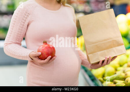 Donna incinta con il sacchetto di frutti di acquisto al negozio di generi alimentari Foto Stock