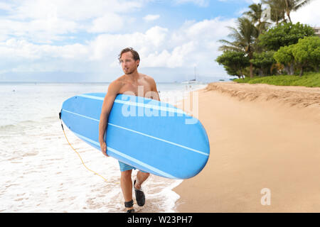 Surfer uomo andando surf sulla spiaggia di Maui HAWAII, Stati Uniti d'America. Professional atleta maschio che trasportano blue surf longboard andando per una sessione di surf sulla spiaggia di Kaanapali, Hawaiian destinazione. Travel surfer lifestyle. Foto Stock