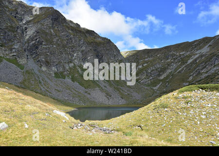 Giornata estiva nel circo del fiume Urdina in alta montagna Rilla, Bulgaria. Luci e ombre sulle ripide colline rocciose che circondano il lago Damga Foto Stock