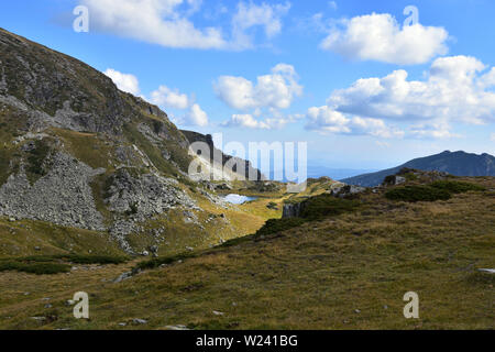 Giornata estiva nel circo del fiume Urdina in alta montagna Rilla, Bulgaria. Luci e ombre sulle colline rocciose di montagna. Lago di Suhoto che splende a distanza Foto Stock