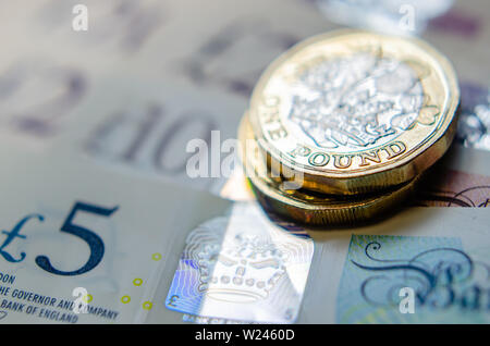 Foto macro di British una libbra di monete sulla parte superiore delle banconote di diverso taglio. Foto Stock