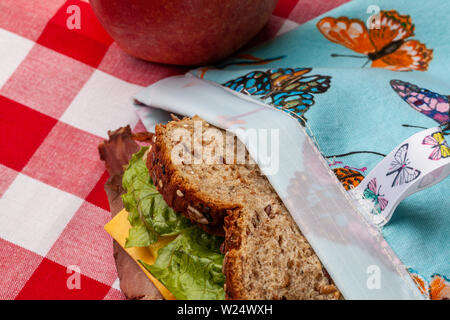 Una mela e un panino in una rispettosa dell'ambiente, in casa, blu riutilizzabili, butterfly borsa sandwich seduti su un rosso e bianco tovaglia a scacchi Foto Stock