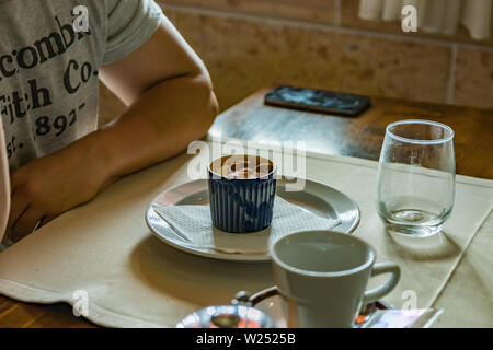 Piccola teiera di metallo con un sacchetto da tè, alcuni bicchieri sul ristorante tavolo. Bianco vapore aumenta al di sopra di acqua calda. Messa a fuoco selettiva. Foto Stock