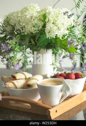 Caffè, rugelach con cioccolato ripieno, fragole e fiori sul vassoio in legno Foto Stock